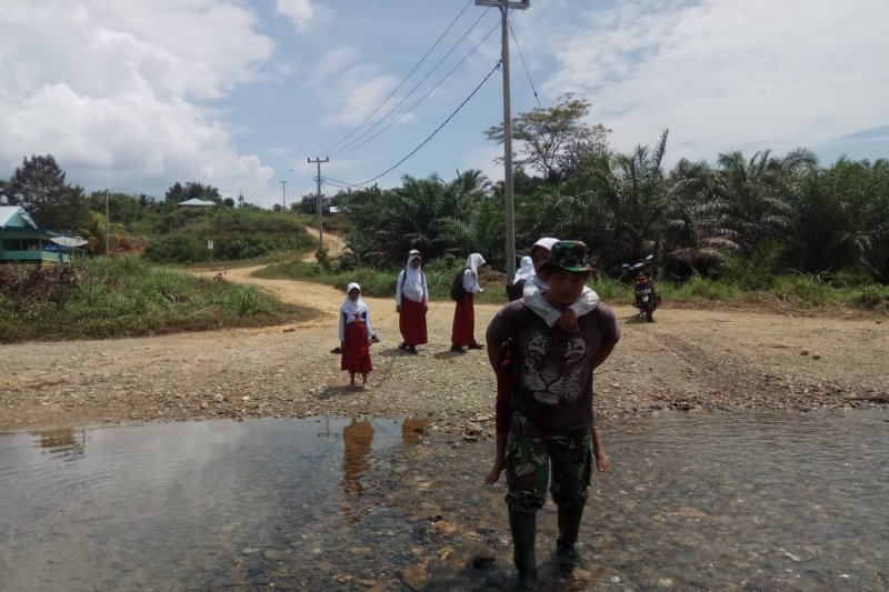 Infrastruktur Terbatas, Prajurit TNI Ini Gendong Murid SD Menyeberangi Sungai